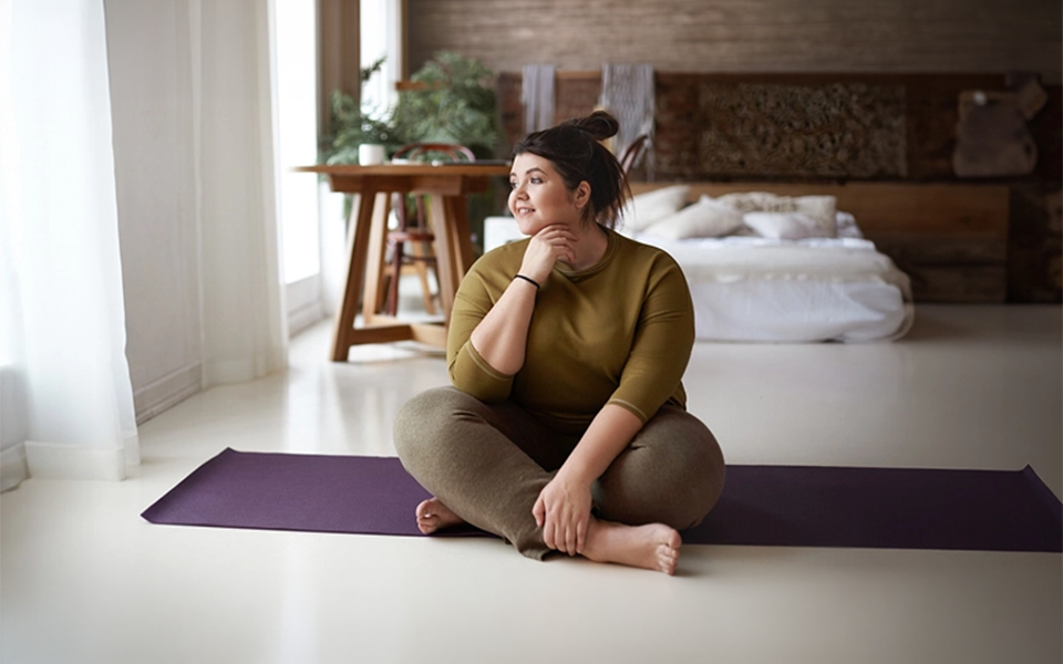 Woman sitting on yoga mat in bedroom